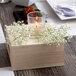 A Leola clear glass votive candle with a flame on a table with flowers.