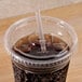 A Fabri-Kal Greenware clear plastic lid with a straw slot on a plastic cup with a straw and a brown liquid.