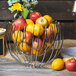 A Clipper Mill chrome plated iron wire basket filled with fruit on a table.