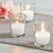 Three Leola clear glass votives with candles on a table.