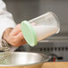 A person using a Cambro green shaker lid to pour white powder into a bowl.