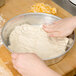 A person kneading American Metalcraft pizza dough in a bowl.