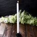 A white Hyoola taper candle in a candle holder on a table.