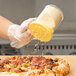 A hand with a yellow Cambro shaker lid sprinkling cheese onto a pizza.