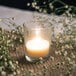 A Leola clear glass votive candle with flowers around it on a table.