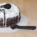 A Mercer Culinary Millennia pie server with a black handle cutting a cake with a cookie on top.