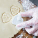 A person wearing plastic gloves uses an Ateco strawberry plunger cookie cutter to cut cookies.