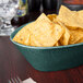 A black oval basket filled with chips on a table in a restaurant.