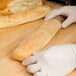 A gloved hand wrapping a baguette in a plastic food bag.