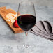 A Chef & Sommelier Cabernet Bordeaux wine glass filled with red wine next to a strawberry on a table.