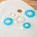 A blue plastic Ateco Carnation cutter with blue snowflakes on dough.