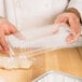 A chef holding a clear plastic dome lid over a tray of dough.