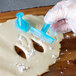 A person using a blue plastic Ateco lily petal cutter to cut dough.