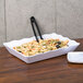 A white rectangular scalloped melamine tray with pasta and olives on it.
