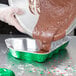 A person wearing a plastic glove pouring brown liquid into a Durable Packaging Christmas tree shaped foil pan.