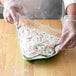 A person in gloves holding a Durable Packaging Christmas tree shaped foil bake pan filled with cake and sprinkles.