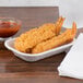 A Huhtamaki Chinet rectangular paper food tray of fried shrimp next to a bowl of sauce on a counter.