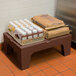 A Cambro brown plastic dunnage rack with brown bags of food and plastic containers on it.
