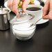 A person pouring sugar from a spoon into an Anchor Hocking glass sugar bowl.