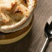 A close-up of French onion soup in a Tuxton two-tone soup crock with a spoon.