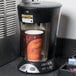 A Bunn My Cafe commercial single cup coffee maker with a paper cup of coffee in it.