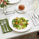 A Landsdale stainless steel dinner fork on a white plate with salad on a table.
