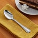 An Acopa Edgewood stainless steel dessert spoon on a napkin next to a slice of cake.
