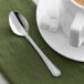 An Acopa Landsdale stainless steel demitasse spoon on a plate with a cup of coffee.