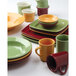 Assorted Tuxton decorated china dinnerware on a table including yellow, green, and red bowls, mugs, and cups.