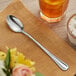 An Acopa Edgeworth stainless steel iced tea spoon on a napkin next to a glass of liquid.