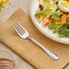 An Acopa Edgeworth stainless steel salad fork on a plate with a salad.