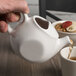 A hand pouring tea into a Tuxton white teapot.