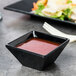 A black GET Siciliano square melamine bowl filled with red sauce.