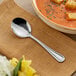 An Acopa Edgeworth stainless steel bouillon spoon on a napkin next to a bowl of soup.