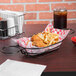 A Clipper Mill black Teflon-coated iron oval basket with fried chicken and french fries on a table.