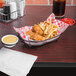 A Clipper Mill black Teflon coated iron oval basket filled with chicken and fries on a table with a red bowl of ketchup.