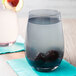 A Stolzle smoky grey stemless wine glass filled with water and blackberries on a white background.