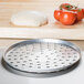 An American Metalcraft aluminum pizza pan with holes filled with dough and tomatoes.