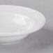 A Libbey Basics Orbis bright white porcelain fruit bowl with a rim on a gray surface.