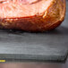 A piece of meat on a Tablecraft black solid cutting board.