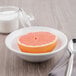 A Libbey Basics white porcelain grapefruit bowl with half a grapefruit and a spoon.