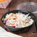 A bowl of coleslaw in a Solo black portion cup with a fork on a table.
