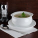 A white bowl of Silver Skillet cream of celery soup with a green leaf in it on a saucer with a spoon.