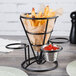 A Clipper Mill black metal cone basket with french fries and ketchup in ramekins.