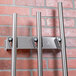 A Matfer Bourgeat stainless steel wall mounted utensil holder rack with 3 hangers on a brick wall.
