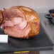 A cooked ham on a Tablecraft black solid cutting board with double wells.
