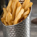 A Tablecraft stainless steel round fry cup filled with French fries on a table.
