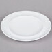 An Arcoroc white porcelain service plate with a rim on a gray surface.