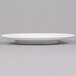 An Arcoroc white porcelain service plate with a rim on a grey surface.