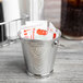 A Clipper Mill stainless steel mini serving pail with a handle holding condiment packets.